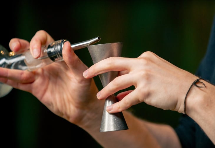 Bartender measuring liquor with jigger.