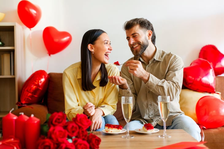 Happy Valentine's Day. Couple in love eating cakes, sitting on sofa in decorated room