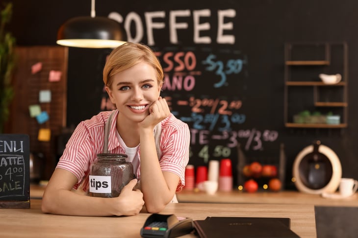 Young female barista with tip jar at table in cafe