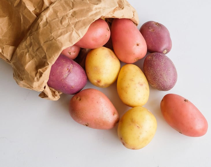 A paper bag full of different colored potatoes.