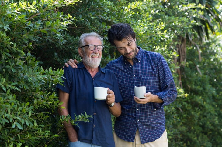 Older man drinking tea on walk with son