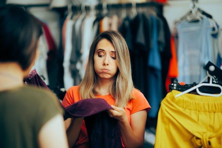 Woman disappointed with the poor quality of clothing item in a thrift store.