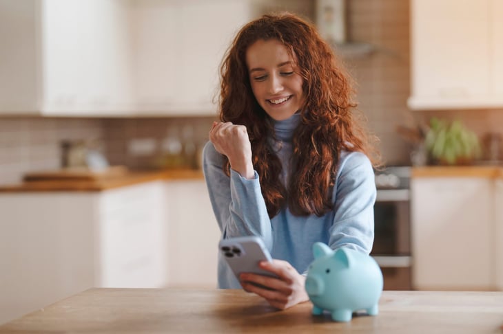 Excited woman with a piggy bank looking at her phone.