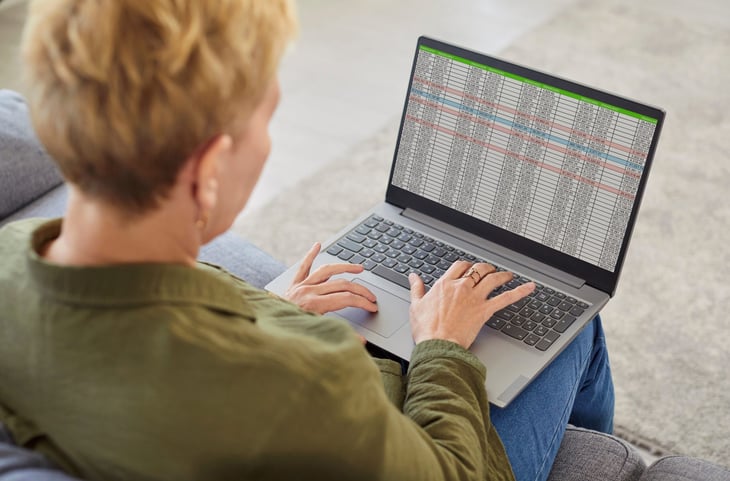 Older woman sitting on sofa and looking through spreadsheet data on laptop screen