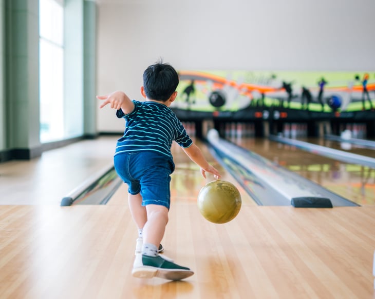Child tossing a bowling ball at a bowling alley