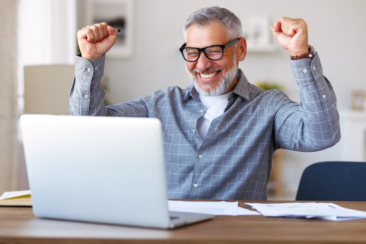 Excited senior man working on taxes before a laptop.
