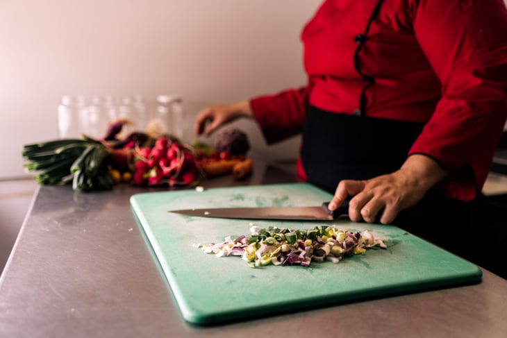 Chef chopping vegetables on a plastic cutting board.