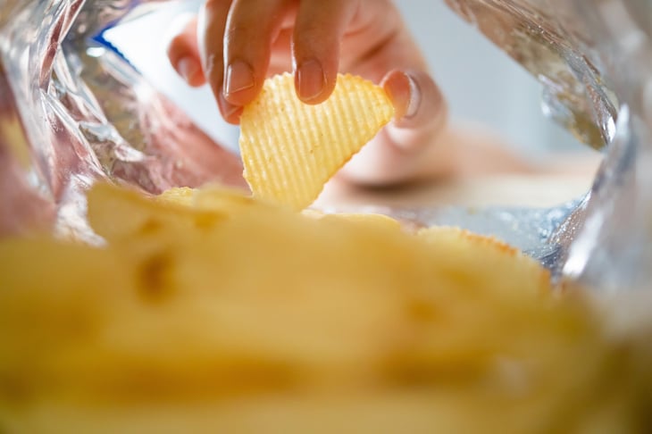 Hand grabbing a rippled potato chip from a bag