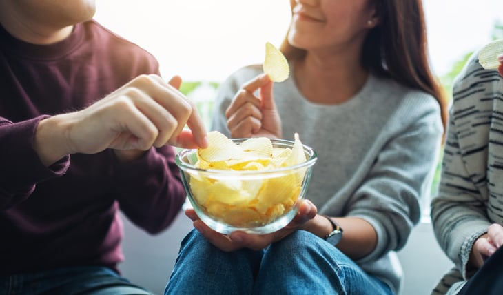 Closeup image of friends sharing and eating potato chips at home party together