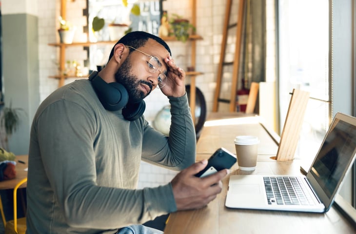 Man working remotely, stressed out. Holding phone.