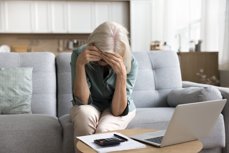 Distressed older woman in front of bills and laptop.