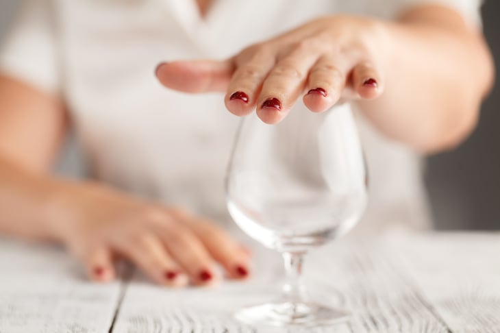 Closeup of woman's hand over a wine glass as she refuses a drink.