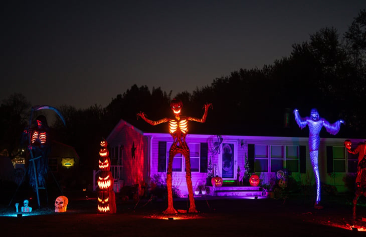 Halloween night house exterior with spooky decor. Scary skeleton in front yard. Home decorated with creepy lanterns and pumpkins.