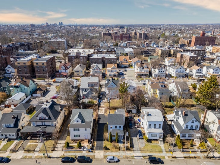 Aerial view of Mount Vernon, New York, showcasing residential homes under blue skies with distant views of New York City