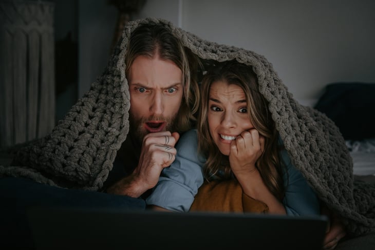 Terrified young couple covered with blanket and watching a horror movie