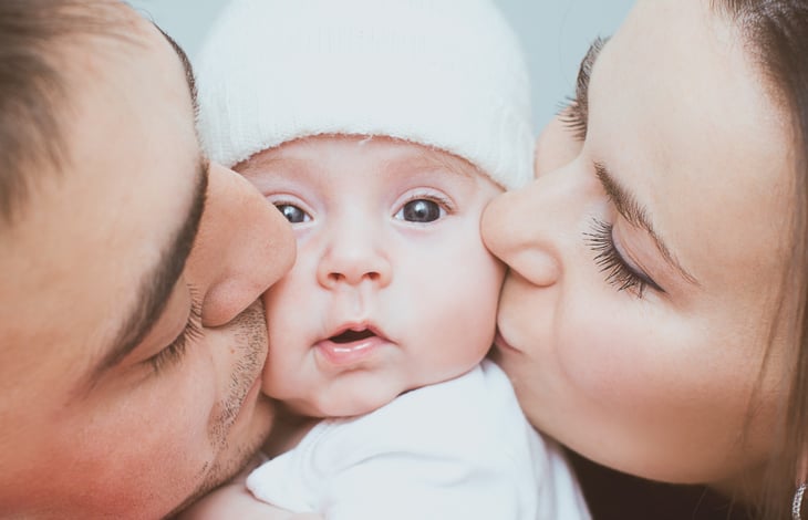 Parents kiss a baby's cheeks