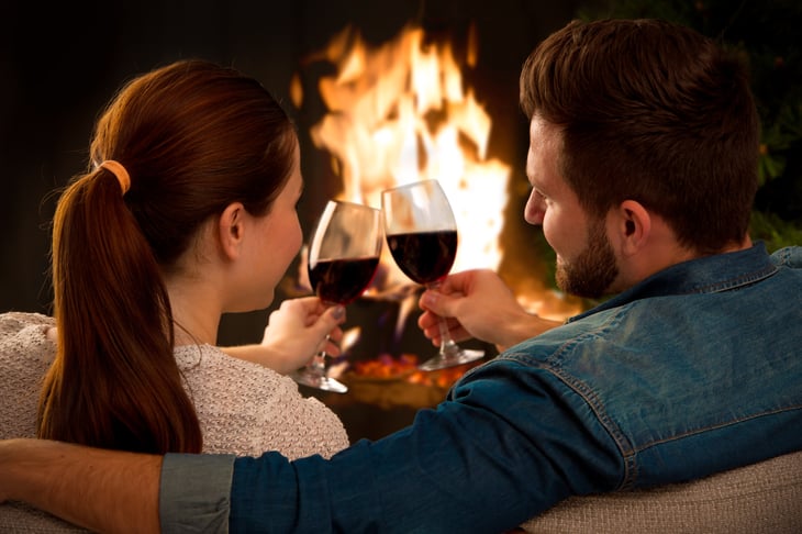 a couple relaxes in front of a fireplace with wine