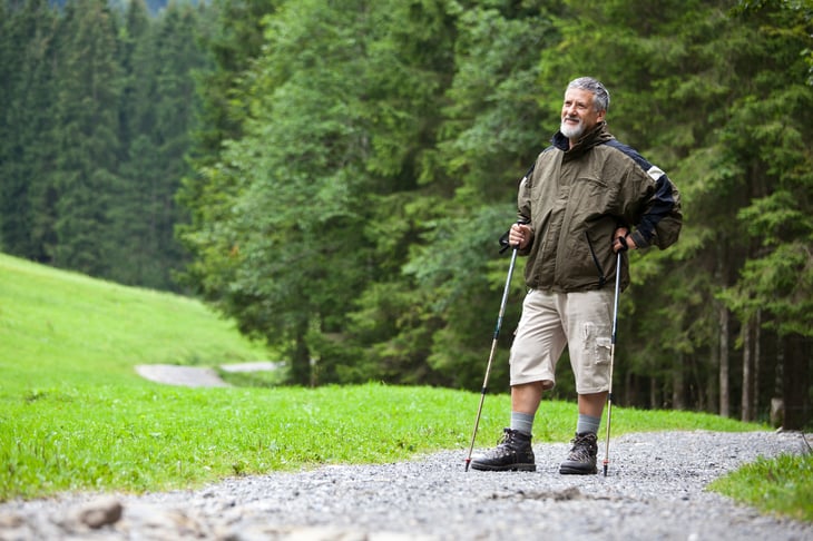 A senior man walks on a trail through woods
