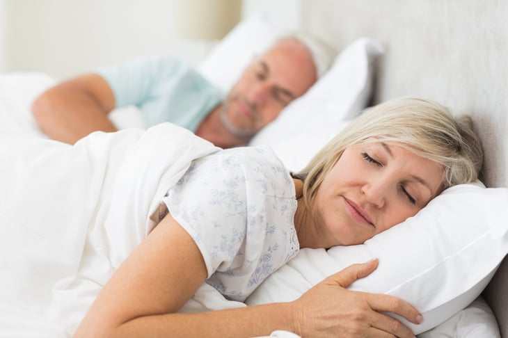 An older couple sleep in a bed