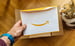 Hand holding an Amazon envelope or package while pet cat looks up